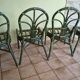 Round rattan table with glass top and 4 green rattan chairs.