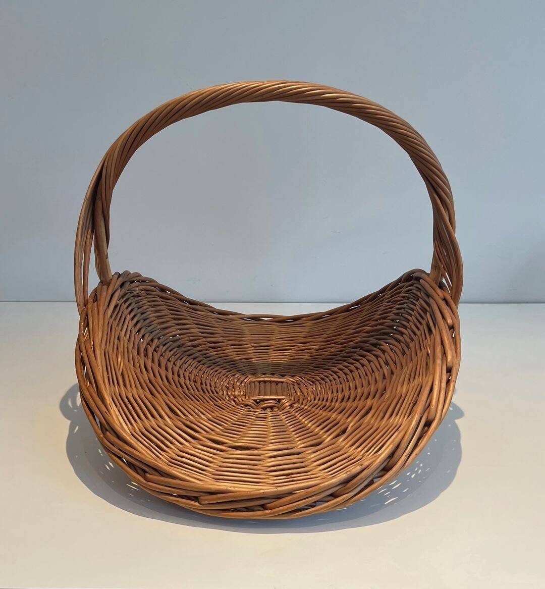 Woven Rattan Log Holder in a Semi-Round Shape with a Central Arched Handle.