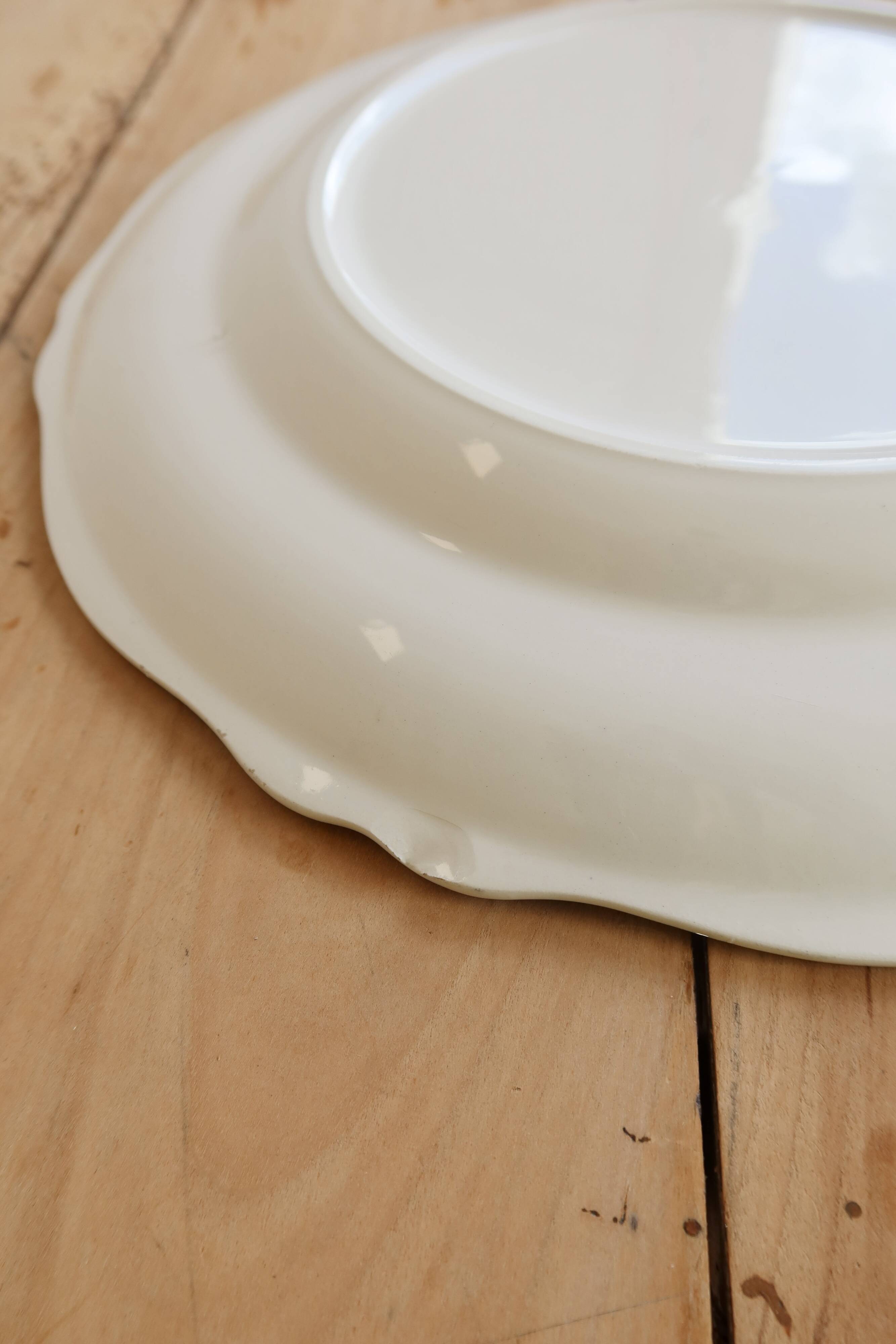 Round vintage ivory earthenware serving dish with scalloped rim.
