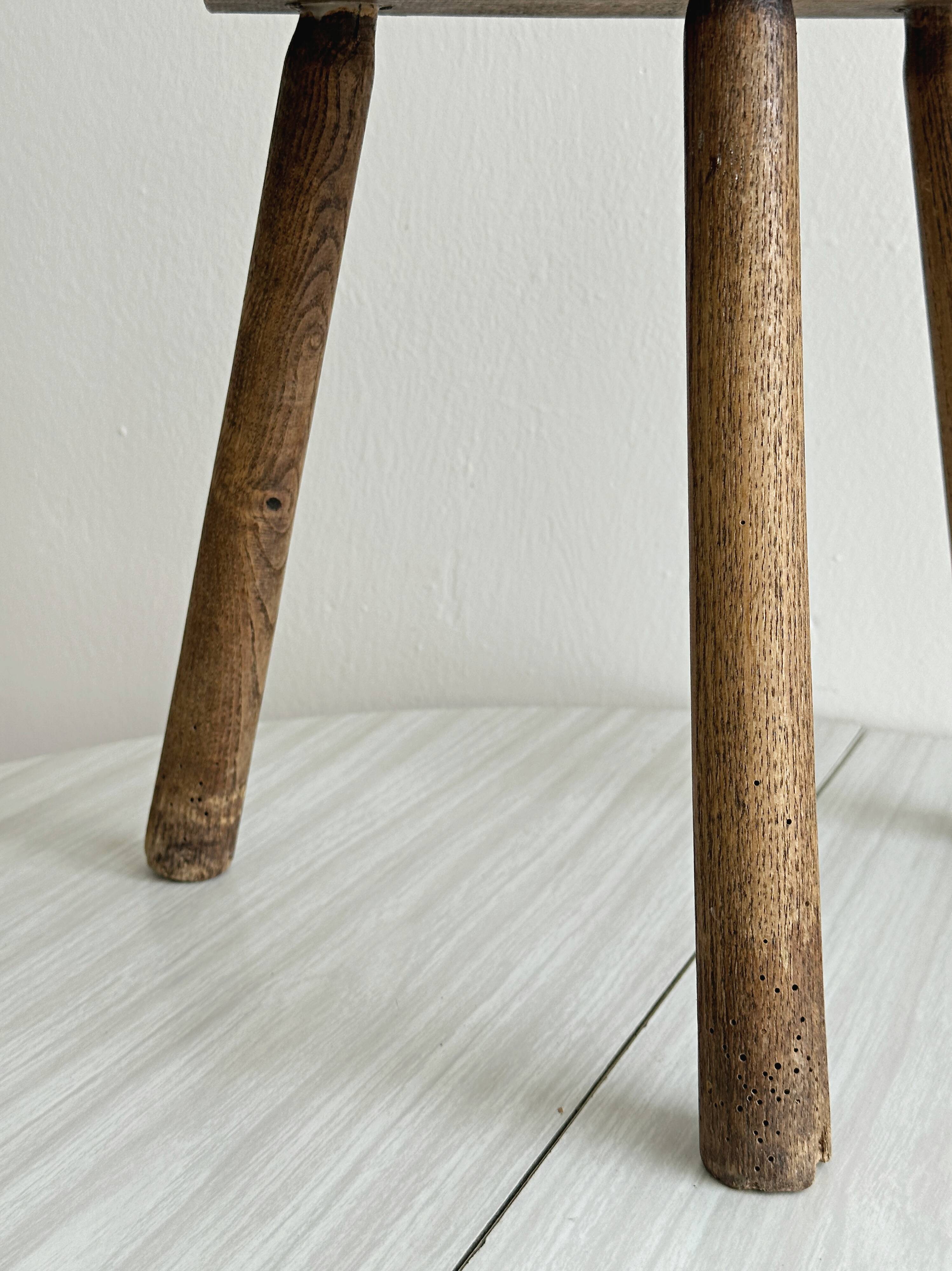 Small antique tripod stool in light wood, half-moon seat.