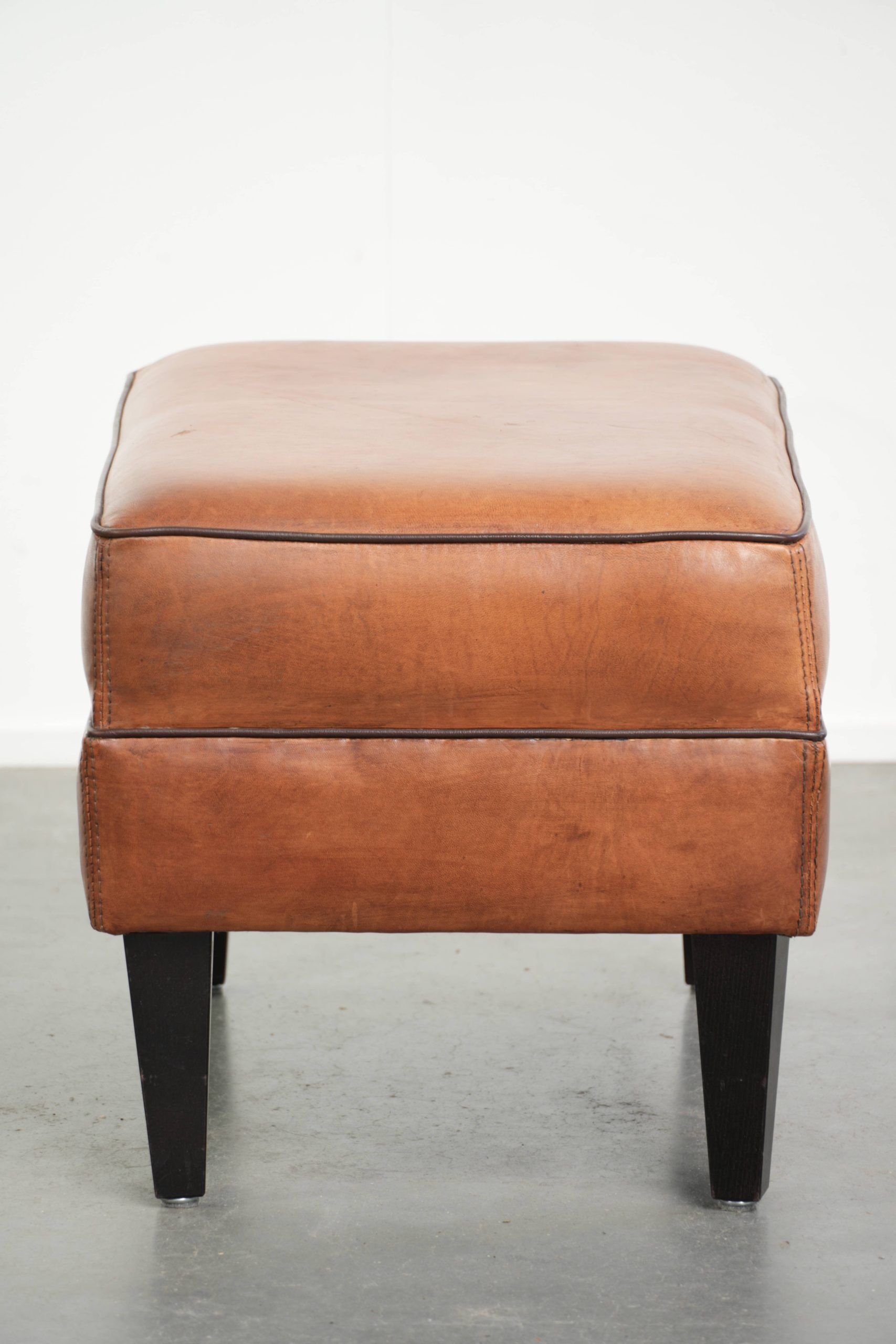 Handy sheepskin ottoman with warm colours finished with black piping