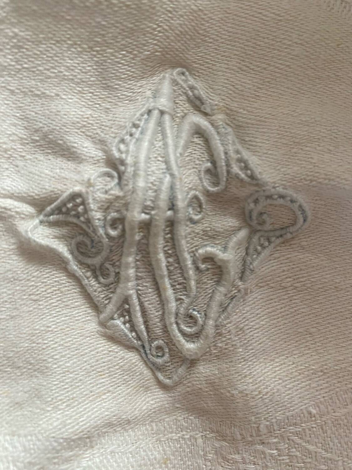 Damask tablecloth with a floral pattern and a central embroidered monogram.