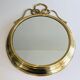 Decorative oval mirror in brass adorned with a large twisted bow.