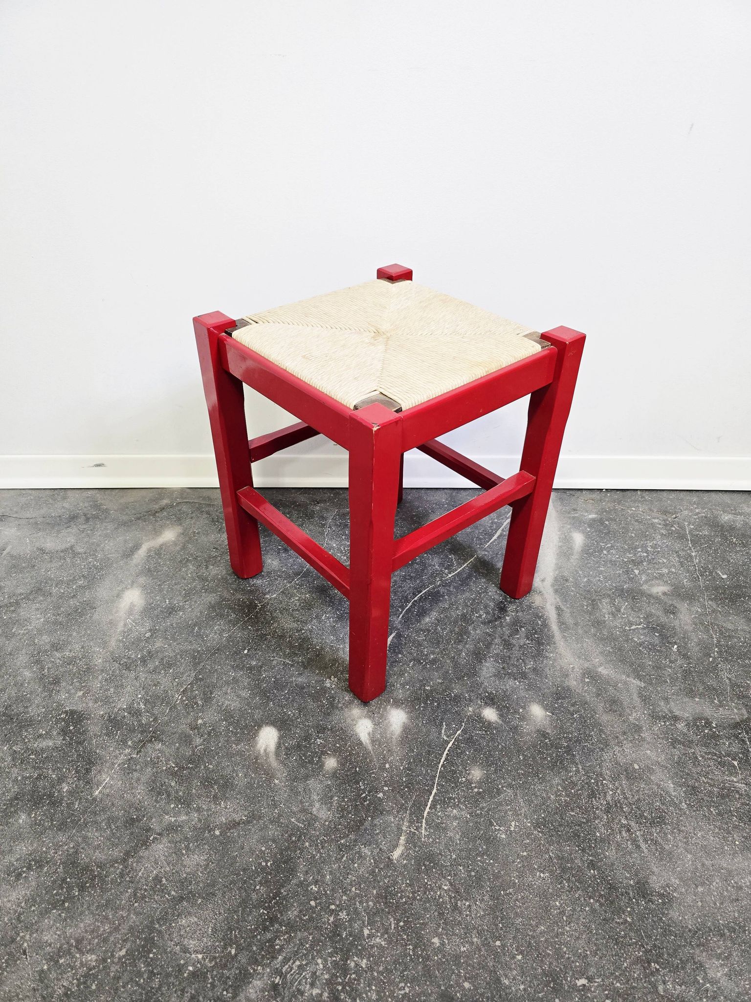 Red wooden stool with a woven straw seat.