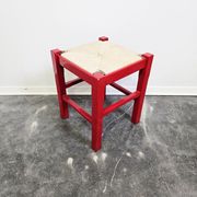 Red wooden stool with a woven straw seat.
