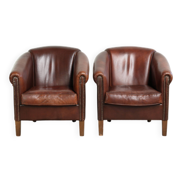 Ensemble de 2 fauteuils club en peau de mouton de couleur cognac foncé.