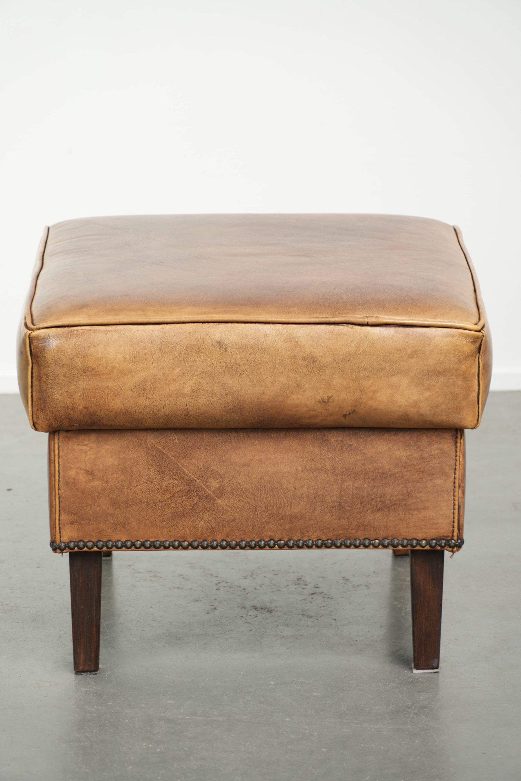 Cowhide ottoman with a beautiful patina finished with decorative nails