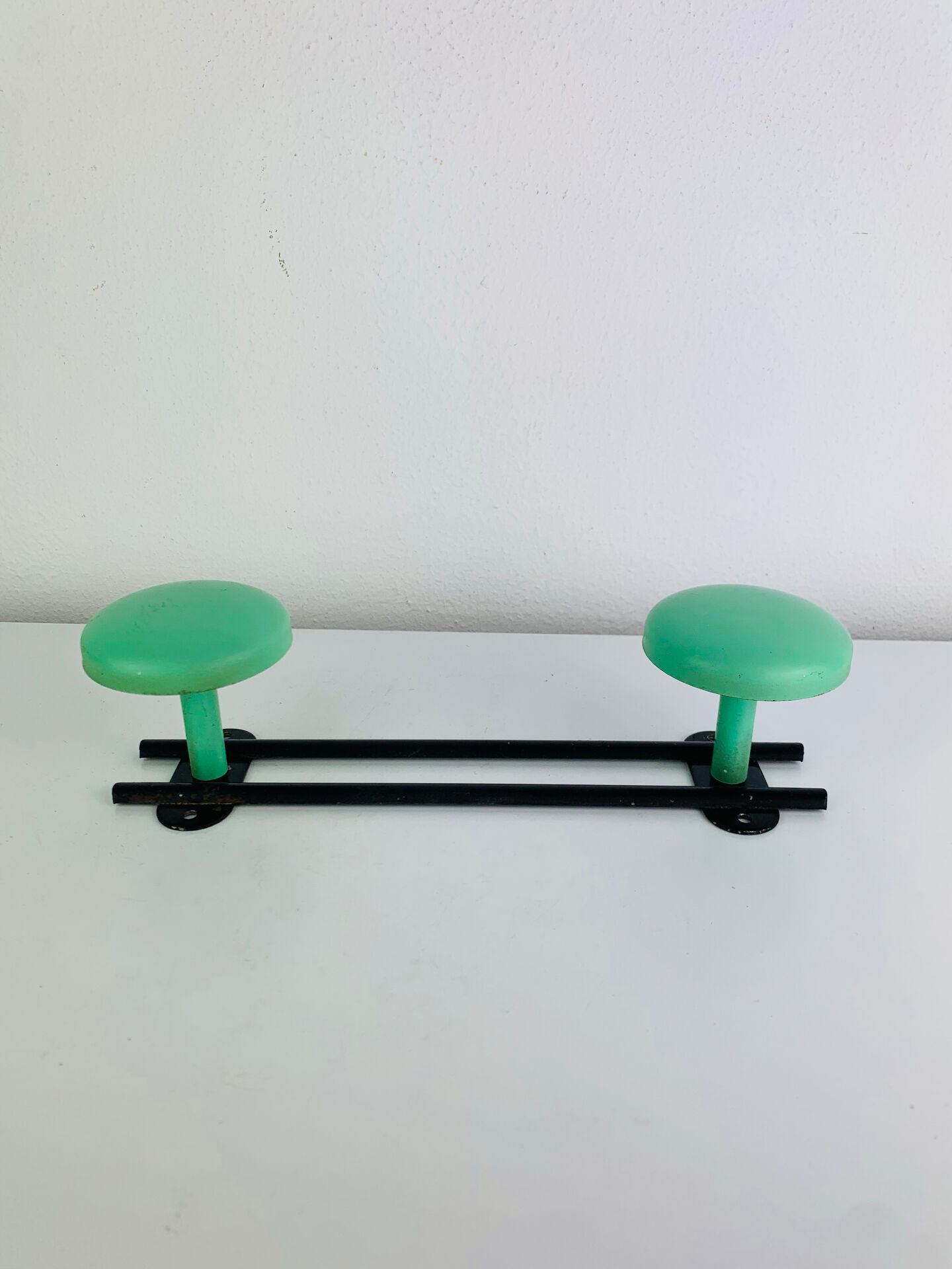 Wall-mounted coat rack with 2 green hooks from the 1950s.