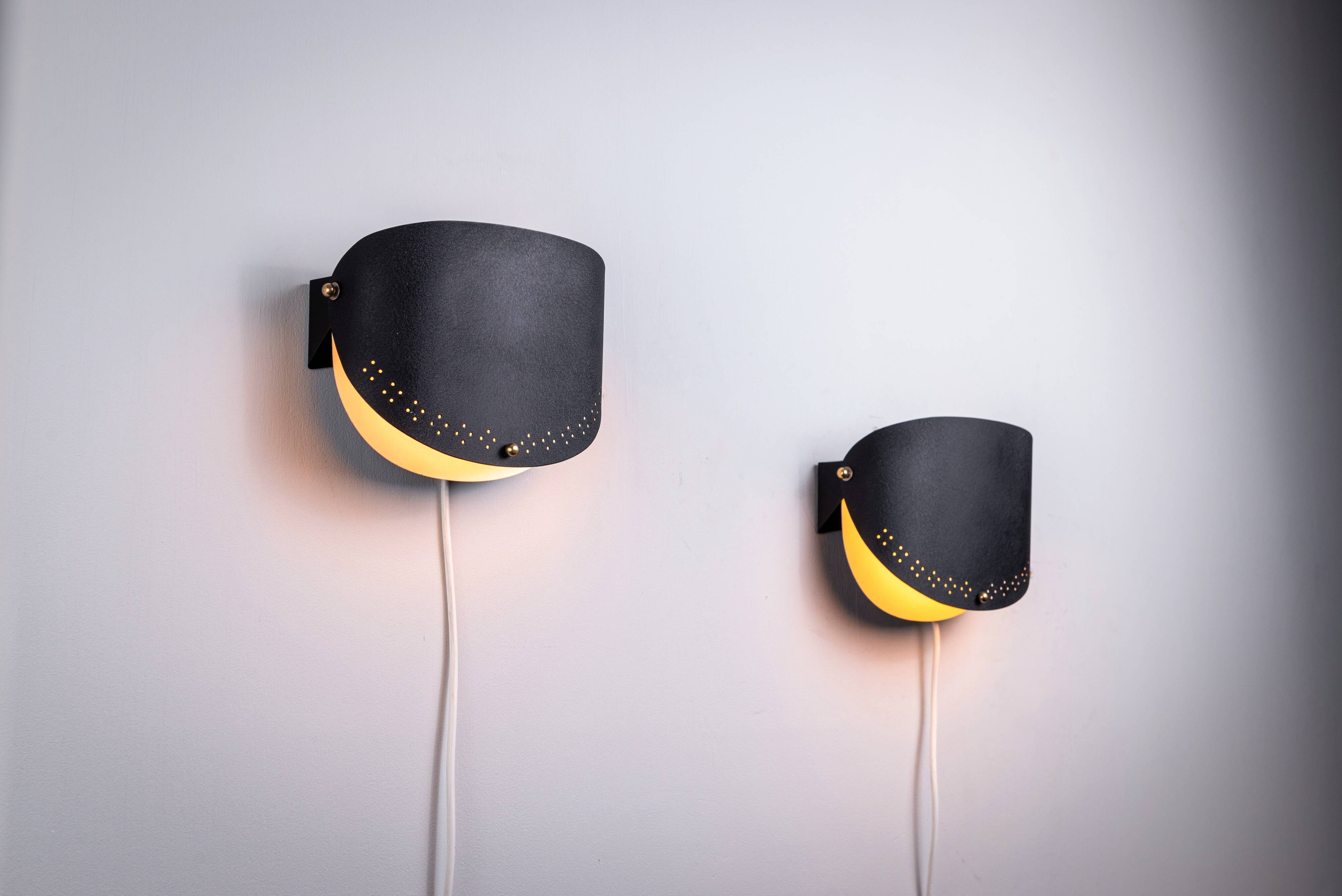 Matte black wall lamps with perforated shades and brass details