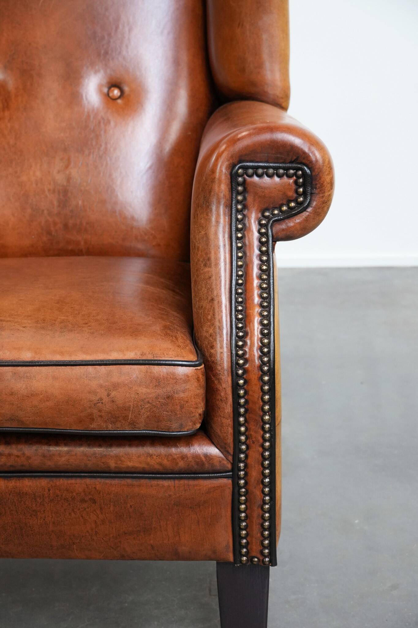Large sheepskin wingback chair with black piping and decorative nails