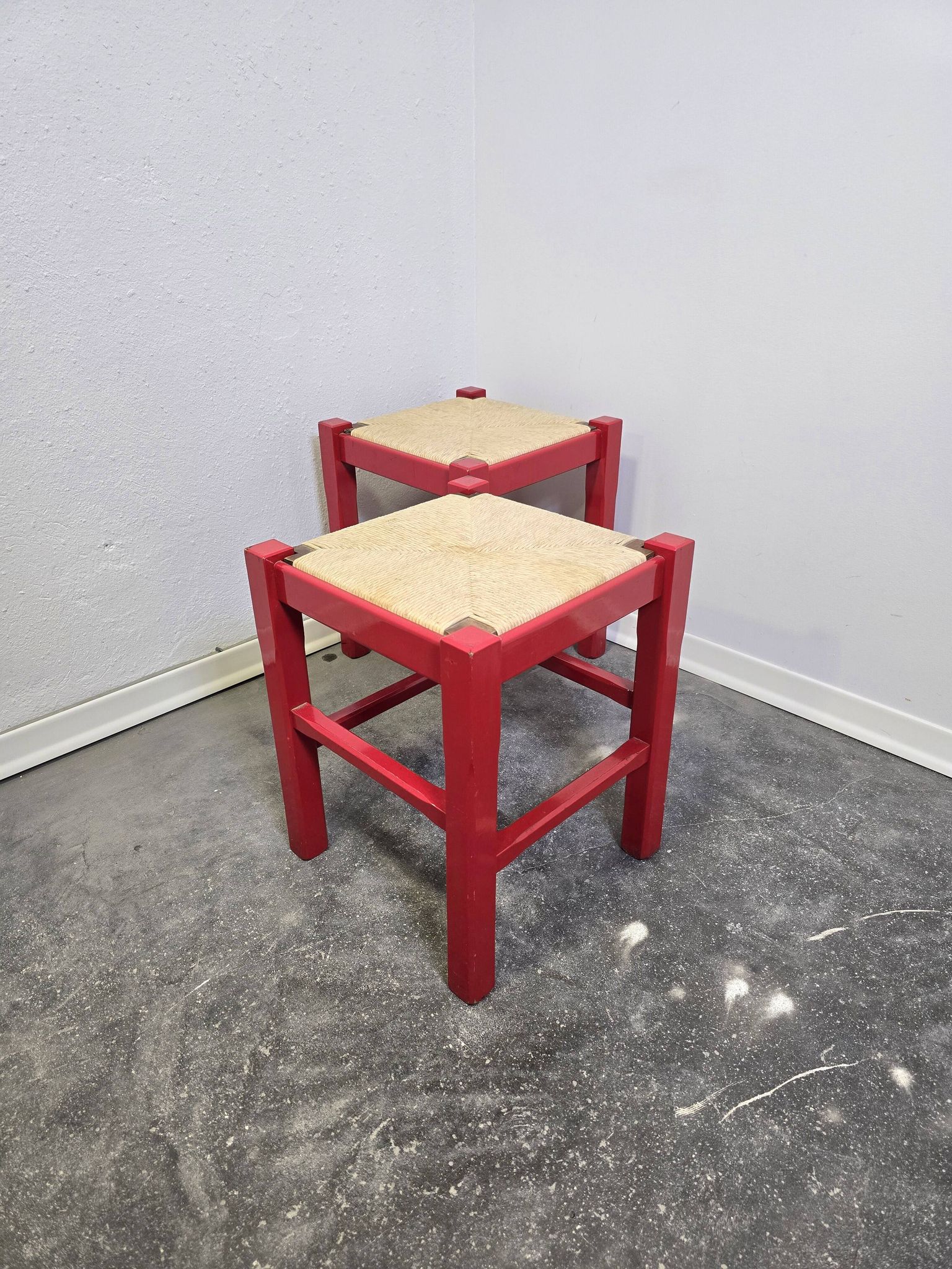 Red wooden stool with a woven straw seat.