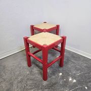 Red wooden stool with a woven straw seat.