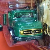 Mercedes flatbed containing drums pulling 1 trailer carrying 1 covered vehicle