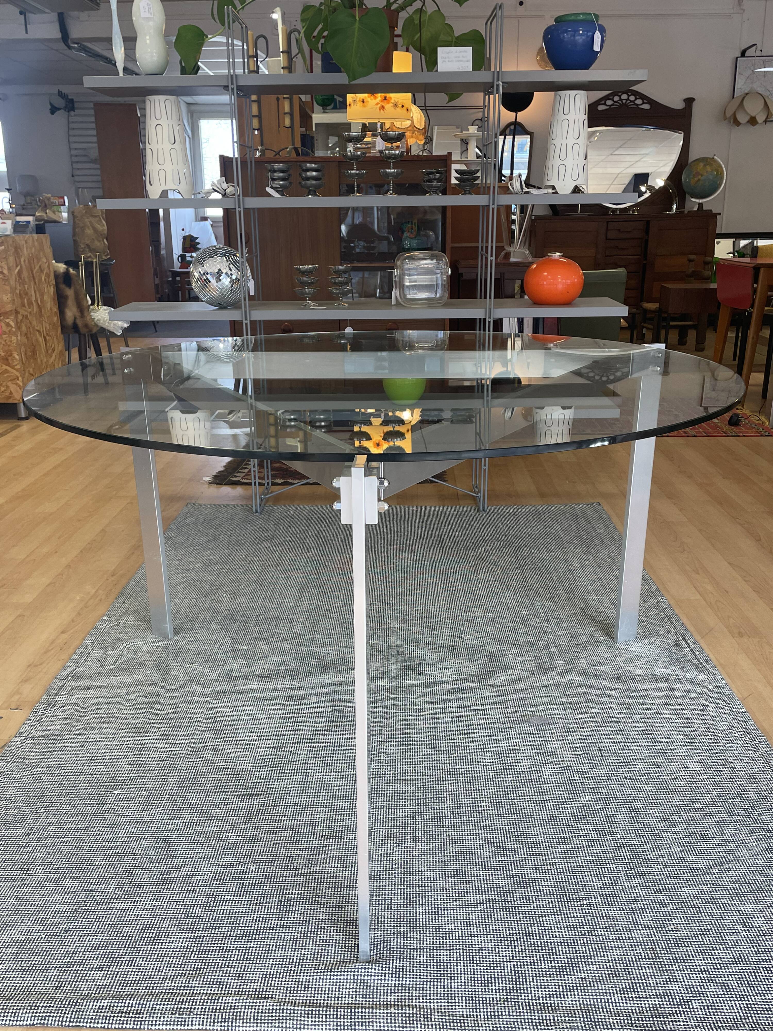 Round dining table with a glass top and brushed metal triangular frame.