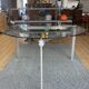 Round dining table with a glass top and brushed metal triangular frame.