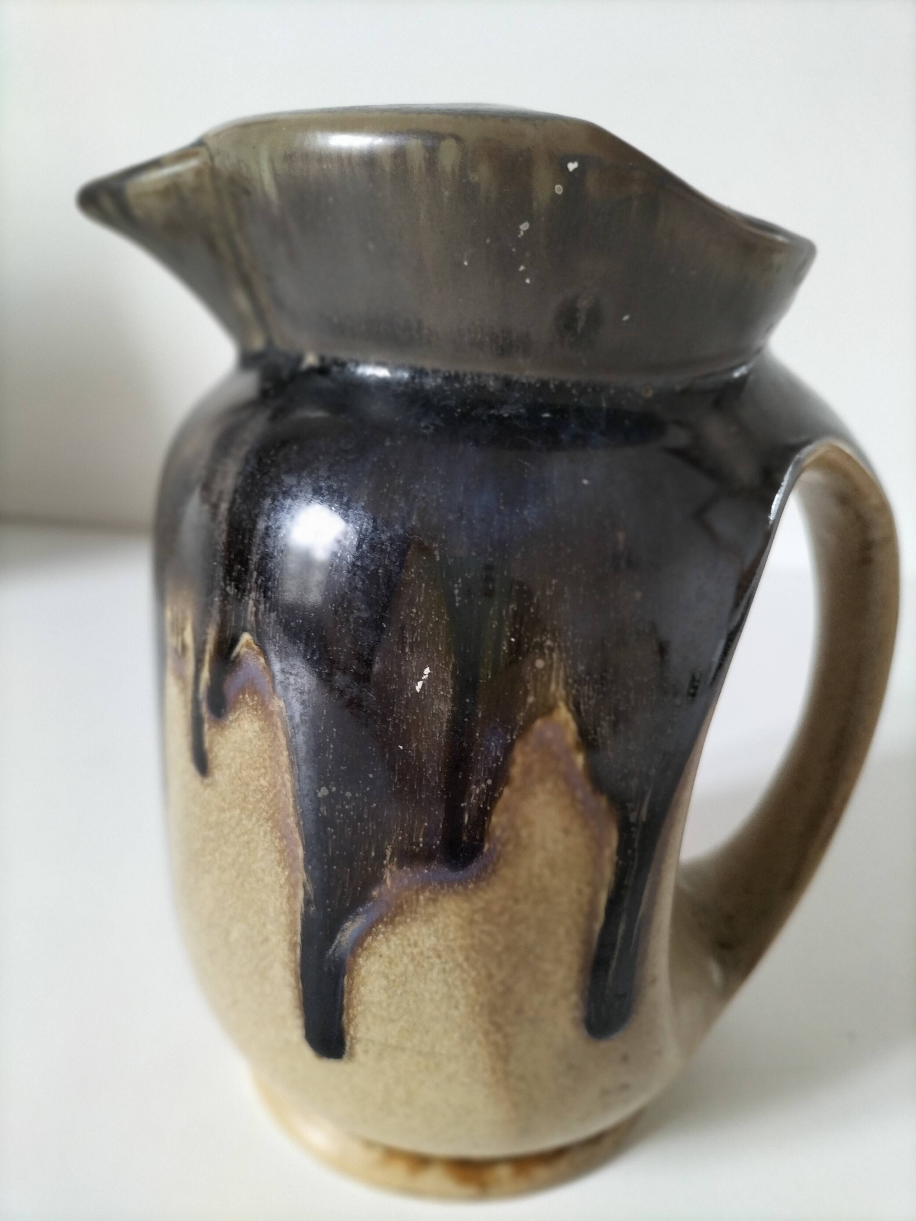 Stoneware jug with deep black drips on a sandy background.
