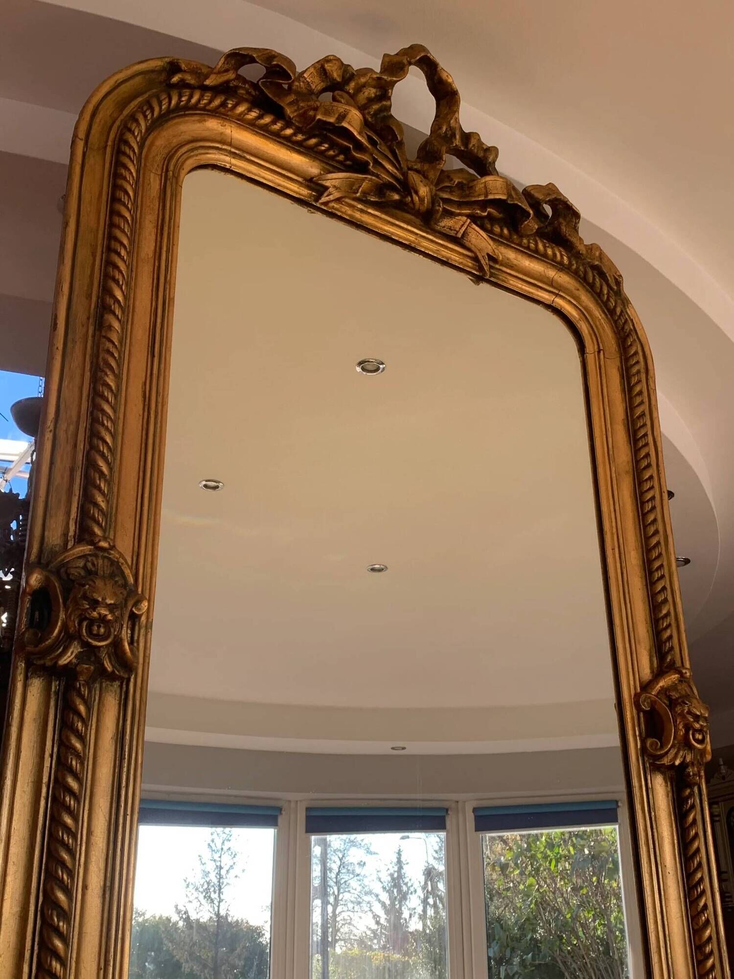 French palace mirror with bow and lion heads, gilded frame.