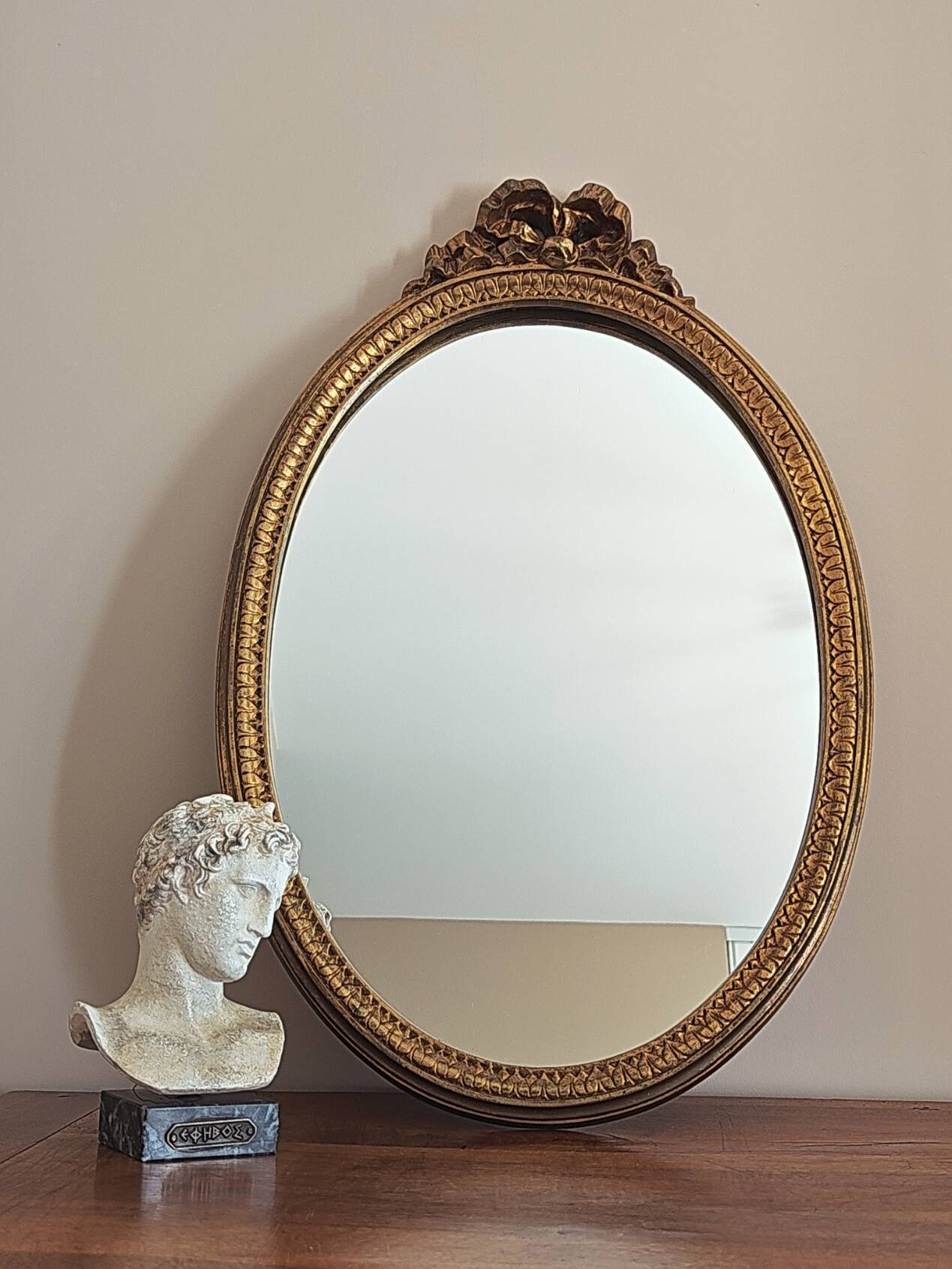 Vintage oval mirror with a carved wooden frame in gold, decorated with a bow.
