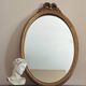 Vintage oval mirror with a carved wooden frame in gold, decorated with a bow.