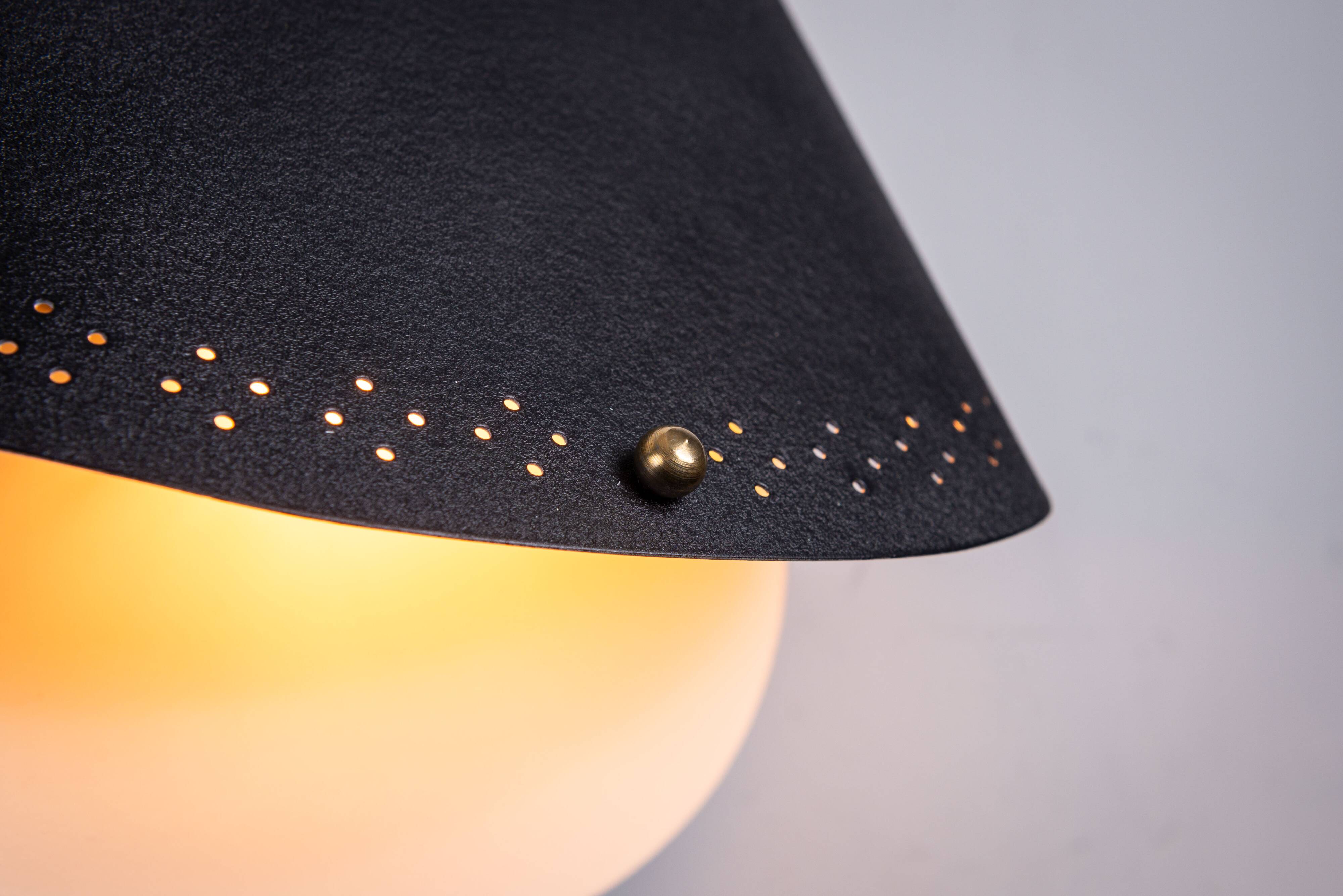 Matte black wall lamps with perforated shades and brass details