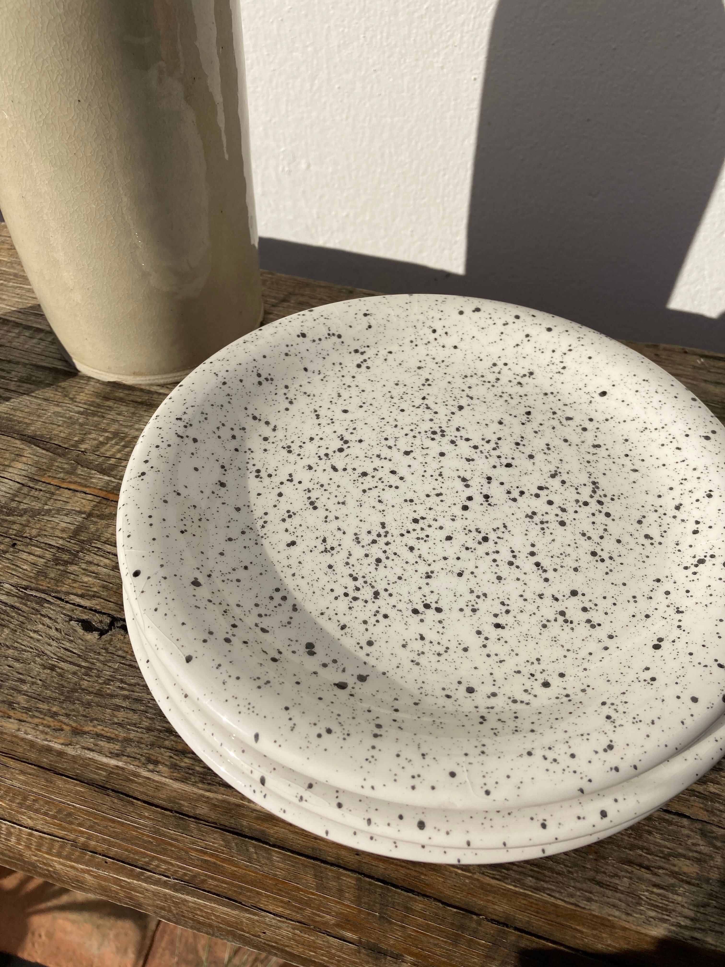 4 black speckled dessert plates on a vintage white background