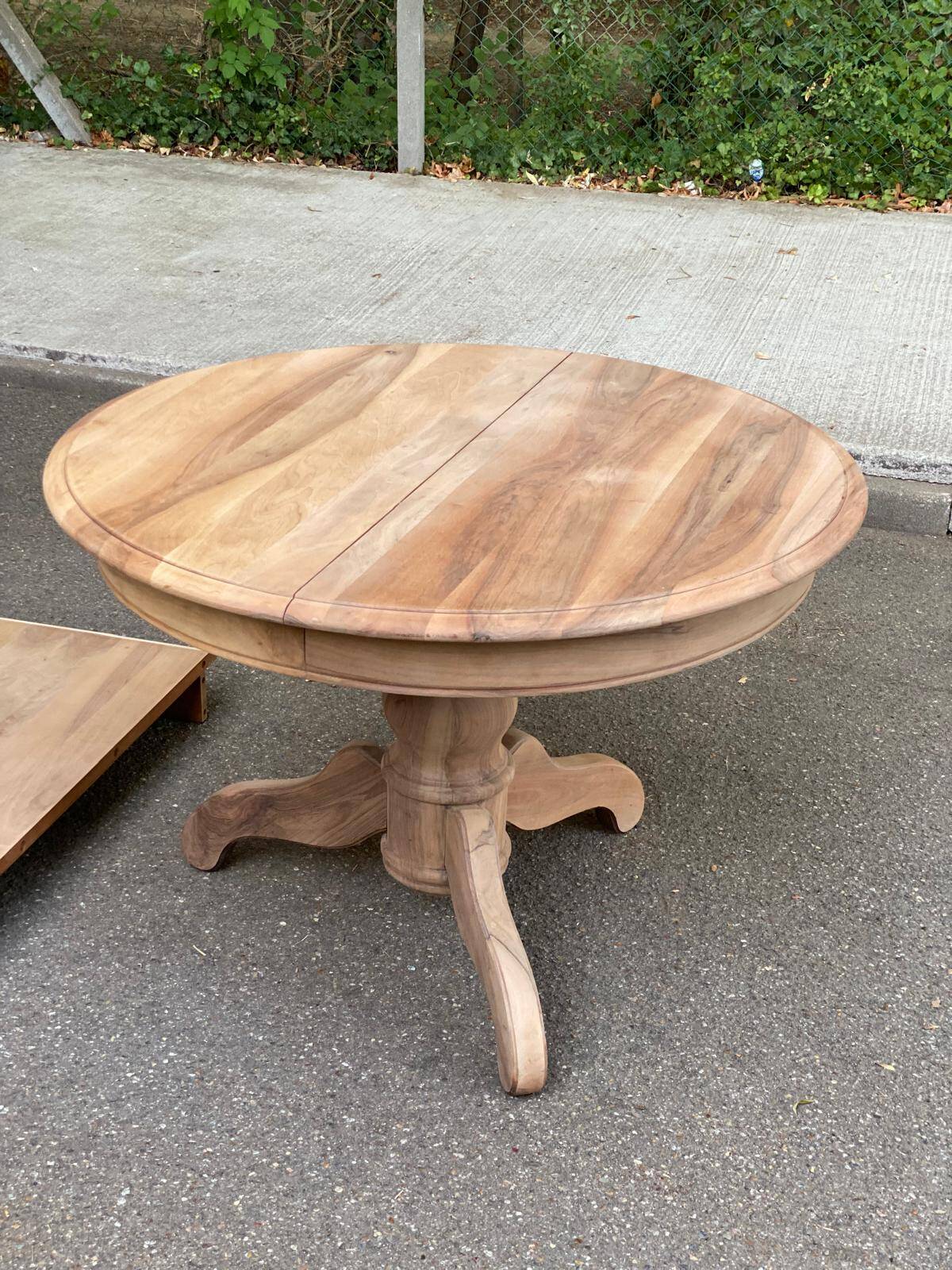 Round extendable dining table stripped in solid raw walnut with a central leg.
