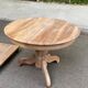 Round extendable dining table stripped in solid raw walnut with a central leg.