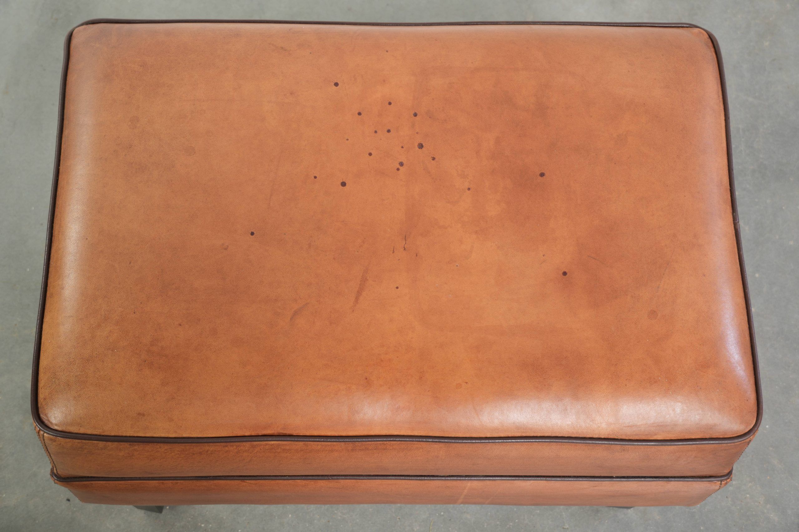 Handy sheepskin ottoman with warm colours finished with black piping