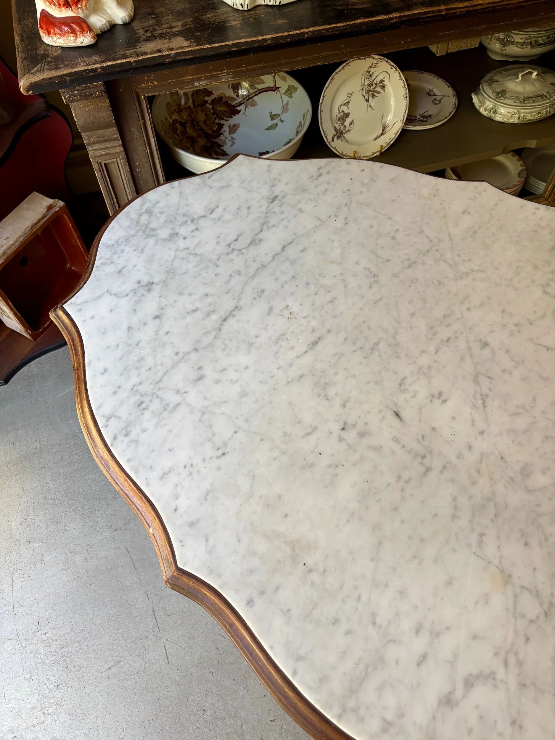 Table with a carved wooden frame and grey marble top on wheels, measuring 130 x 82 cm.