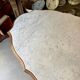 Table with a carved wooden frame and grey marble top on wheels, measuring 130 x 82 cm.