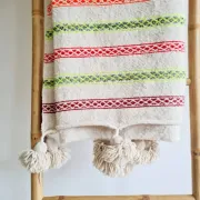 Moroccan plaid made of handwoven wool, decorated with stripes and pom-poms.