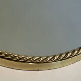 Oval brass mirror surrounded by a cord and adorned