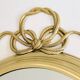 Large decorative oval mirror in brass adorned with a significant twisted bow.