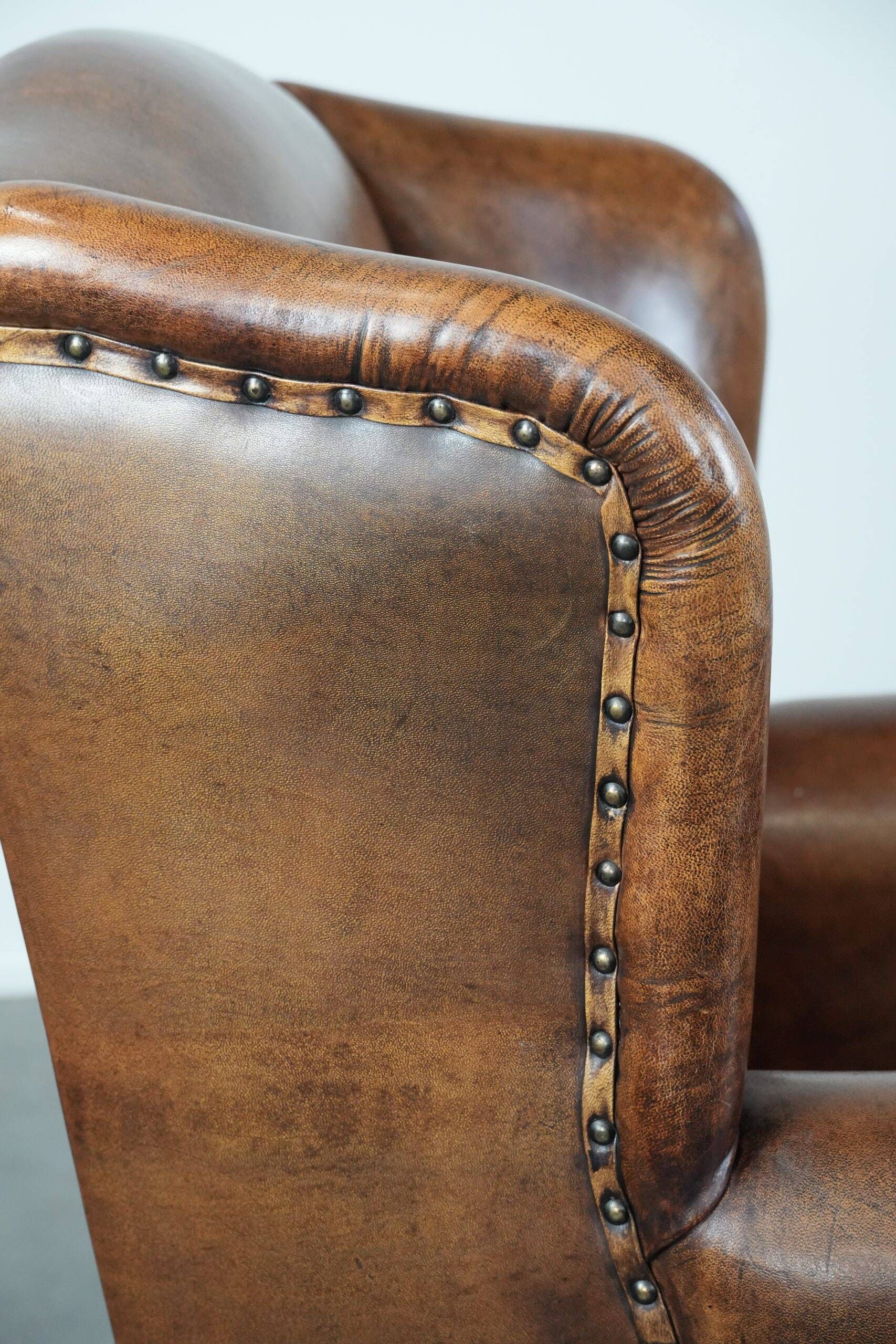 Sheepskin wingback armchair with decorative nails and black piping