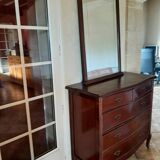 Style set: bevelled mirror and curved wooden chest of drawers.
