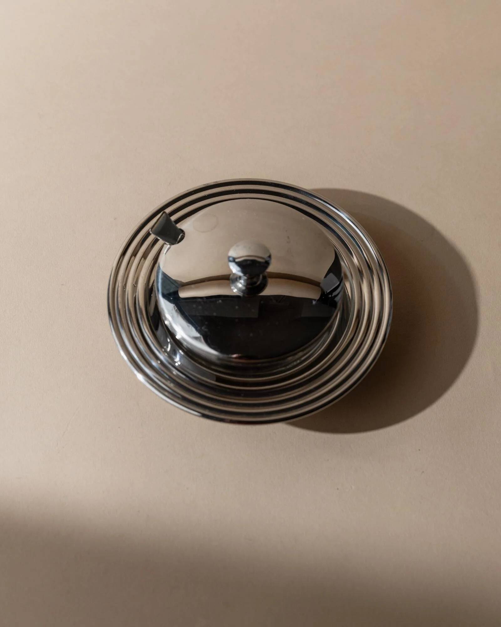 Vintage 1970s condiment pot made of glass and stainless steel with a lid, complete with a matching spoon.