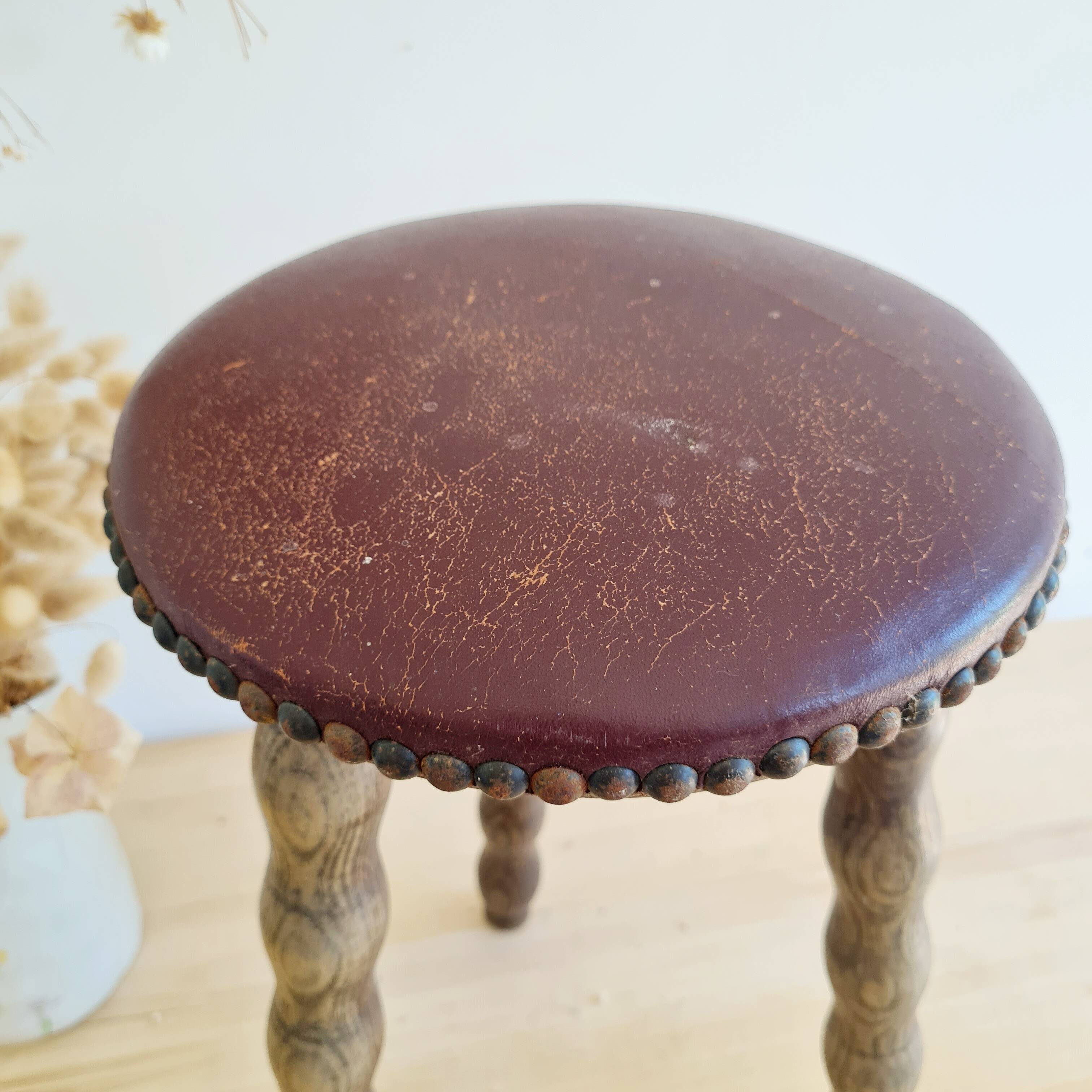 Antique tripod stool with turned wooden legs and leather seat.