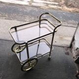 Two-tier bar cart in gold-plated brass with transparent glass shelves, yellow finish.