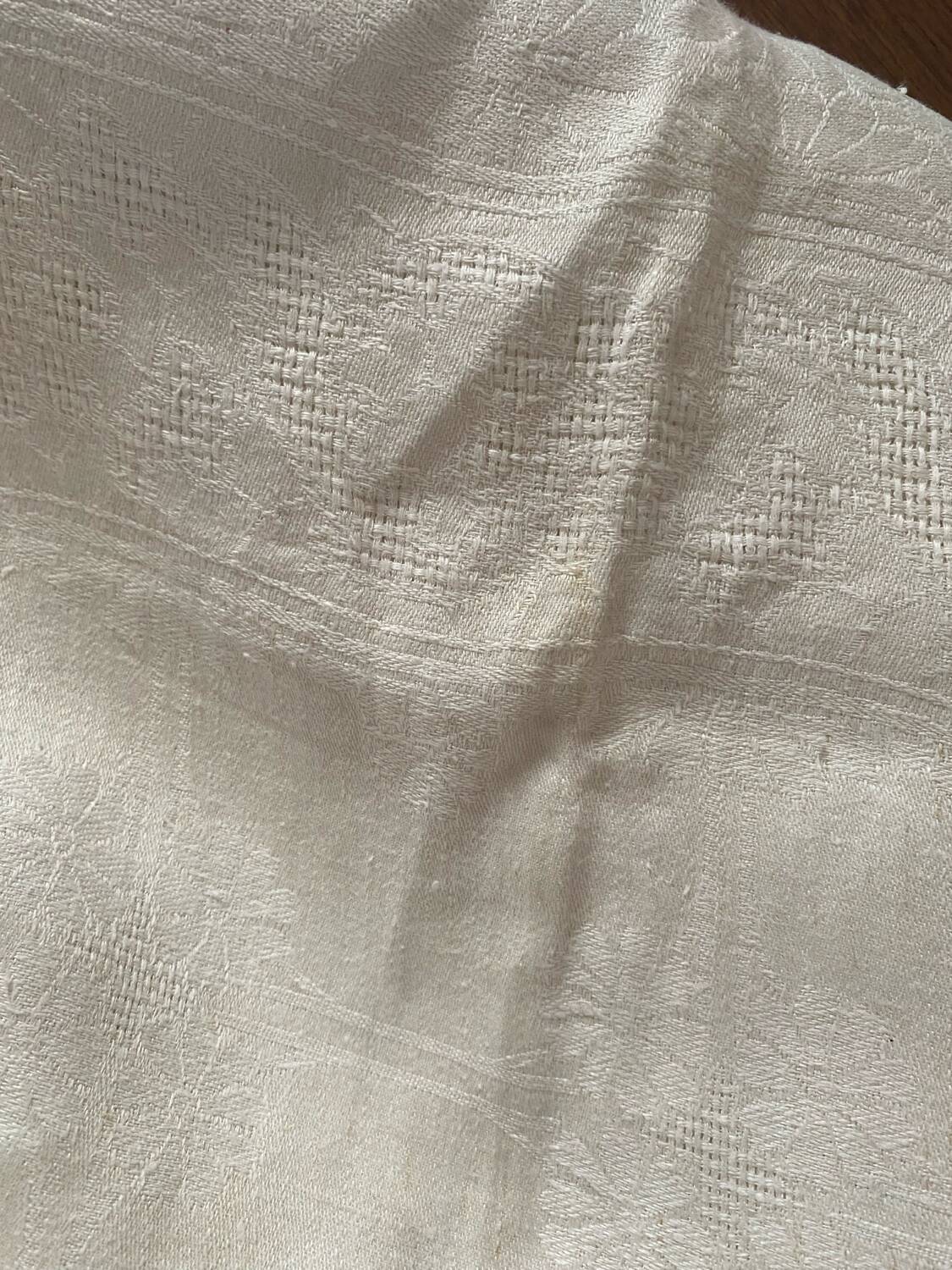 Damask tablecloth with a floral pattern and a central embroidered monogram.