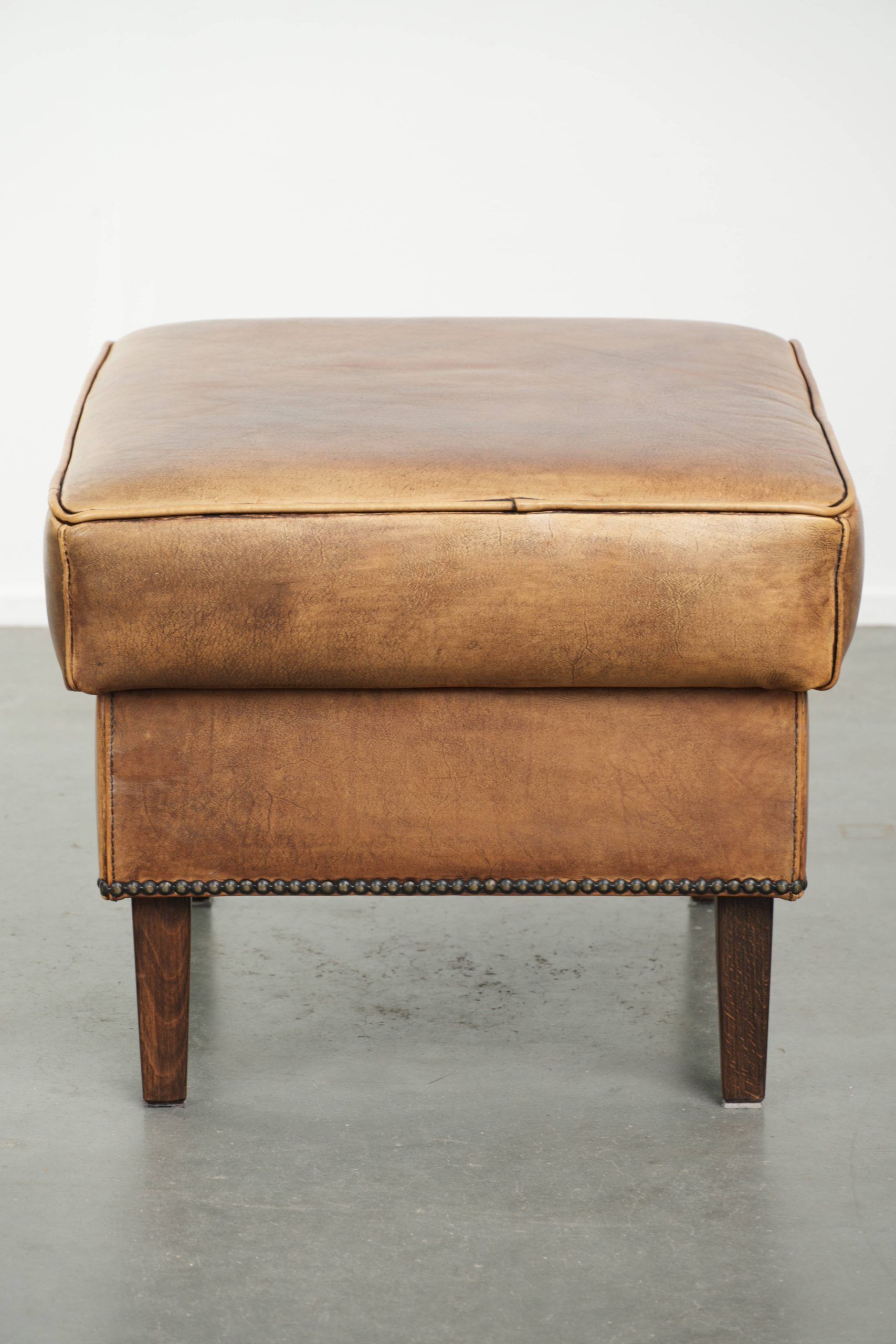 Cowhide ottoman with a beautiful patina finished with decorative nails
