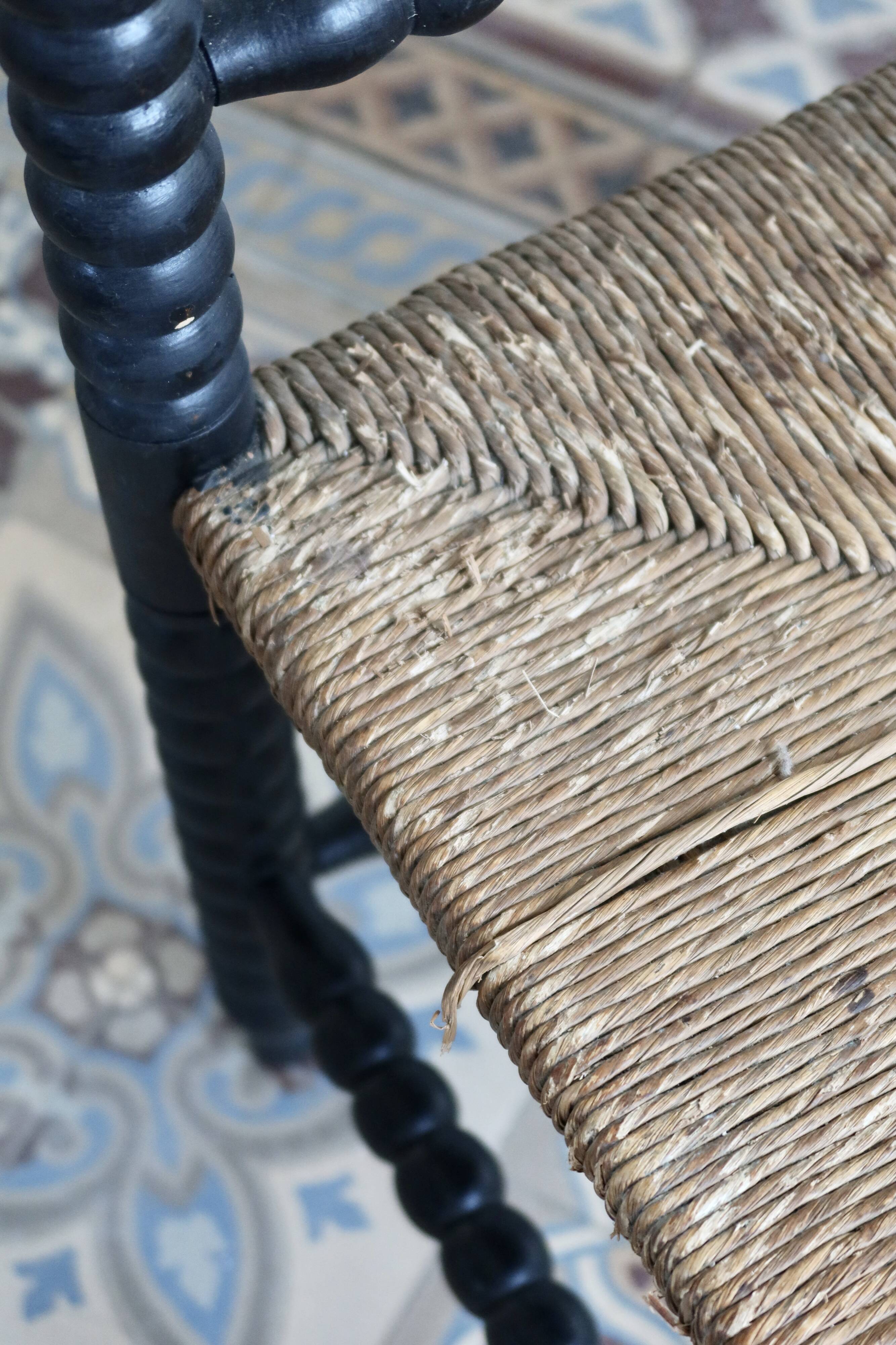 Antique black turned wood corner chair with a straw seat.