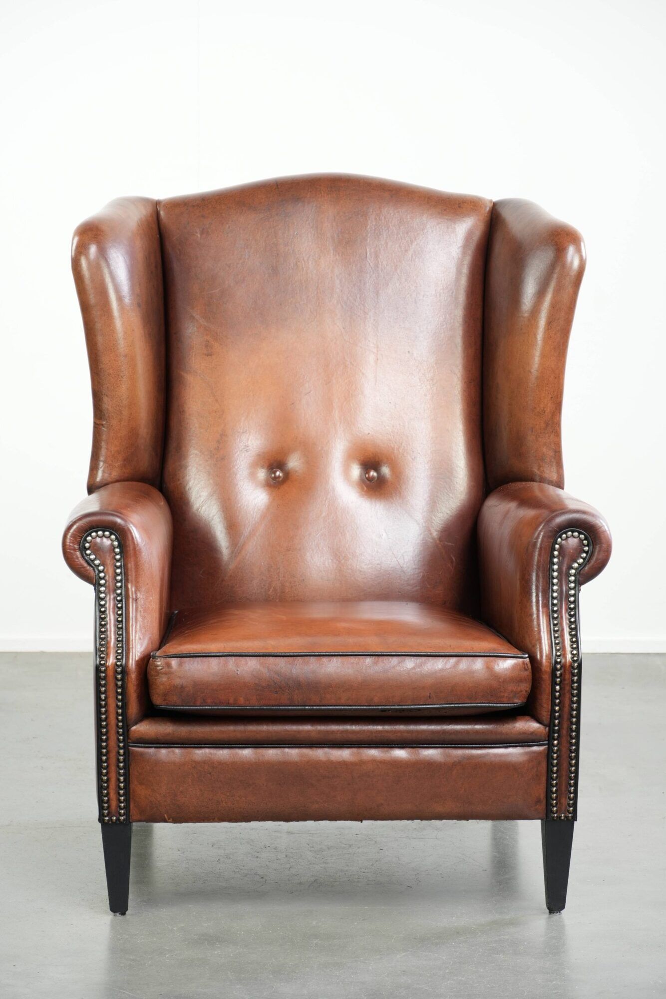 Sheepskin wingback armchair in a warm cognac colour with refined nailhead trim