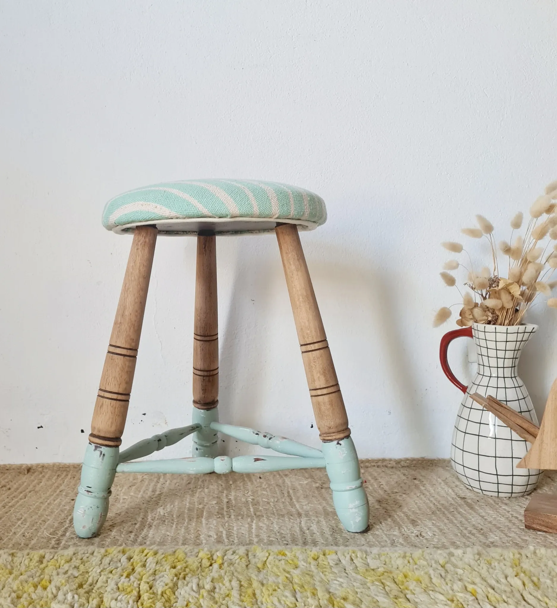 Antique tripod stool with blue striped seat.