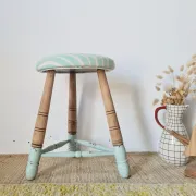 Antique tripod stool with blue striped seat.