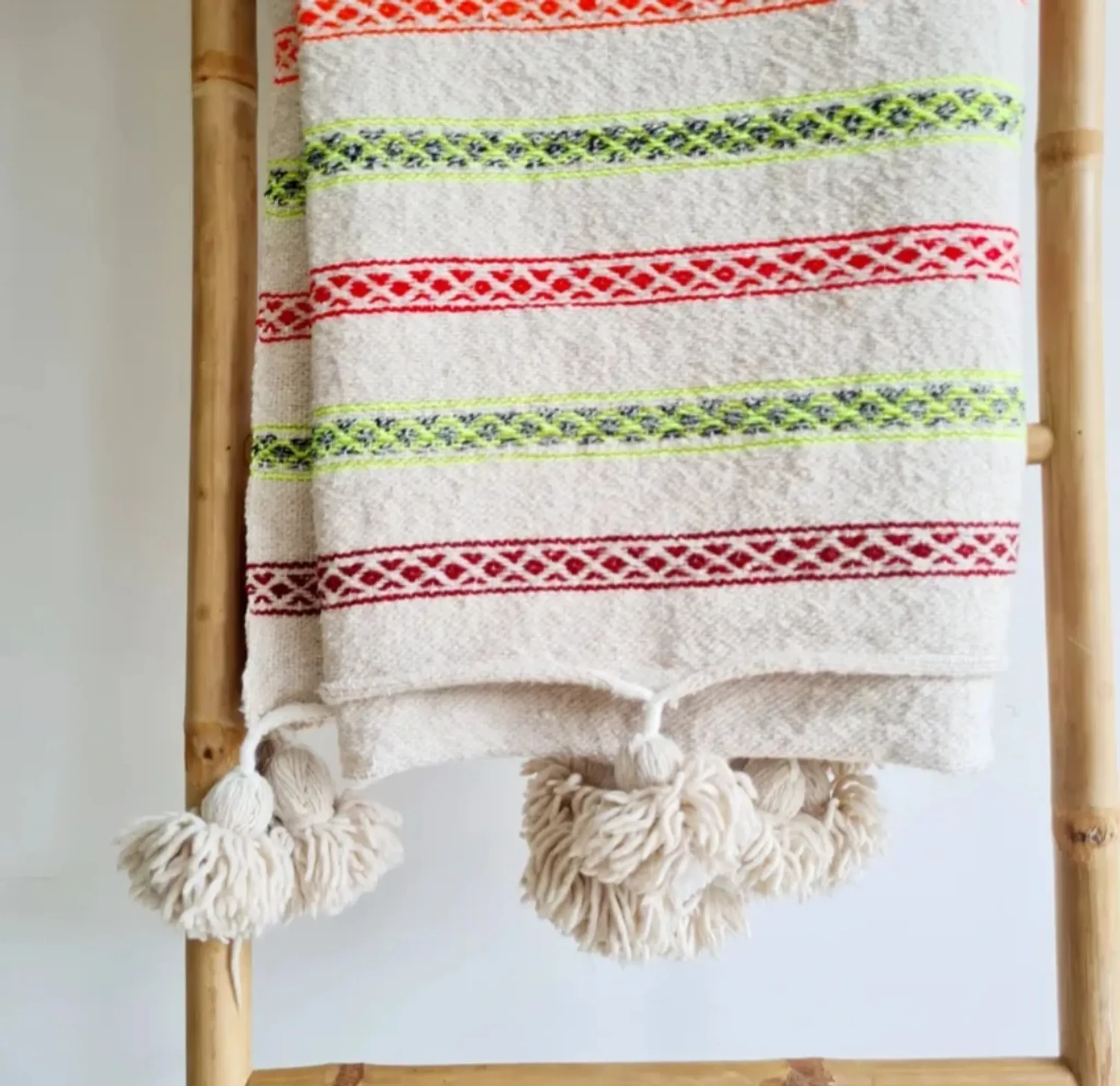 Moroccan plaid made of handwoven wool, decorated with stripes and pom poms.