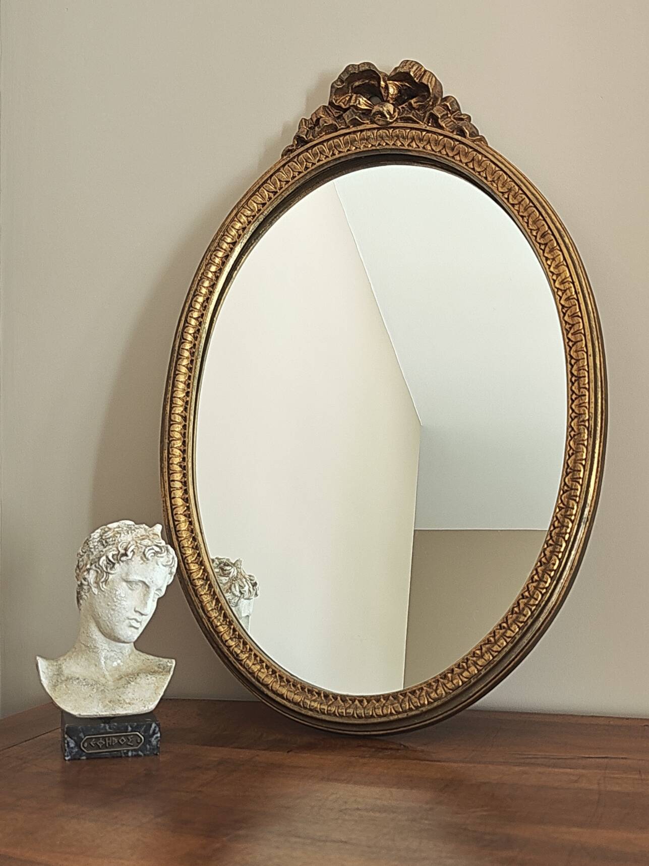 Vintage oval mirror with a carved wooden frame in gold, decorated with a bow.