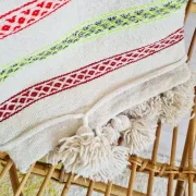 Moroccan plaid made of handwoven wool, decorated with stripes and pom poms.