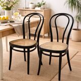 Pair of black curved wooden bistro chairs with caning in Thonet style.