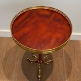 A round, neoclassical-style brass side table with a base decorated with dolphins and a red celluloid top encircled by an openwork gallery, attributed to the House of Jansen.