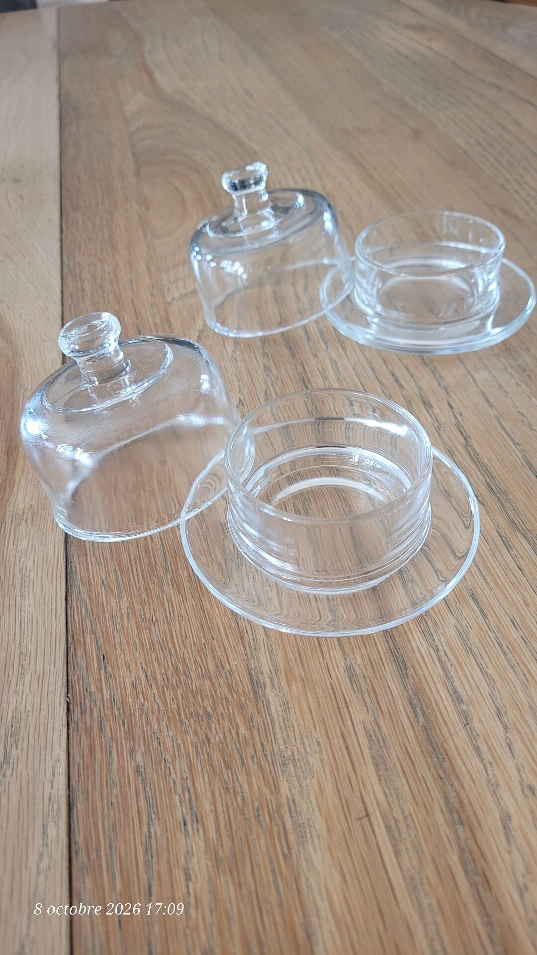 2 transparent glass butter dishes accompanied by their matching cloches.